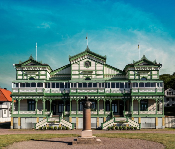 Un hôtel du 19ème siècle avec des pignons ornés, une terrasse et des cadres peints en vert fait face à la mer.