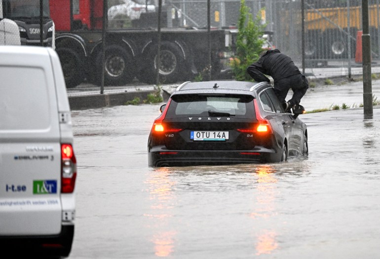 Un homme sort d'une voiture qui a essayé de traverser un rond-point inondé à Arlov sur l'autoroute E6 fermée et inondée près de Malmö, Suède.